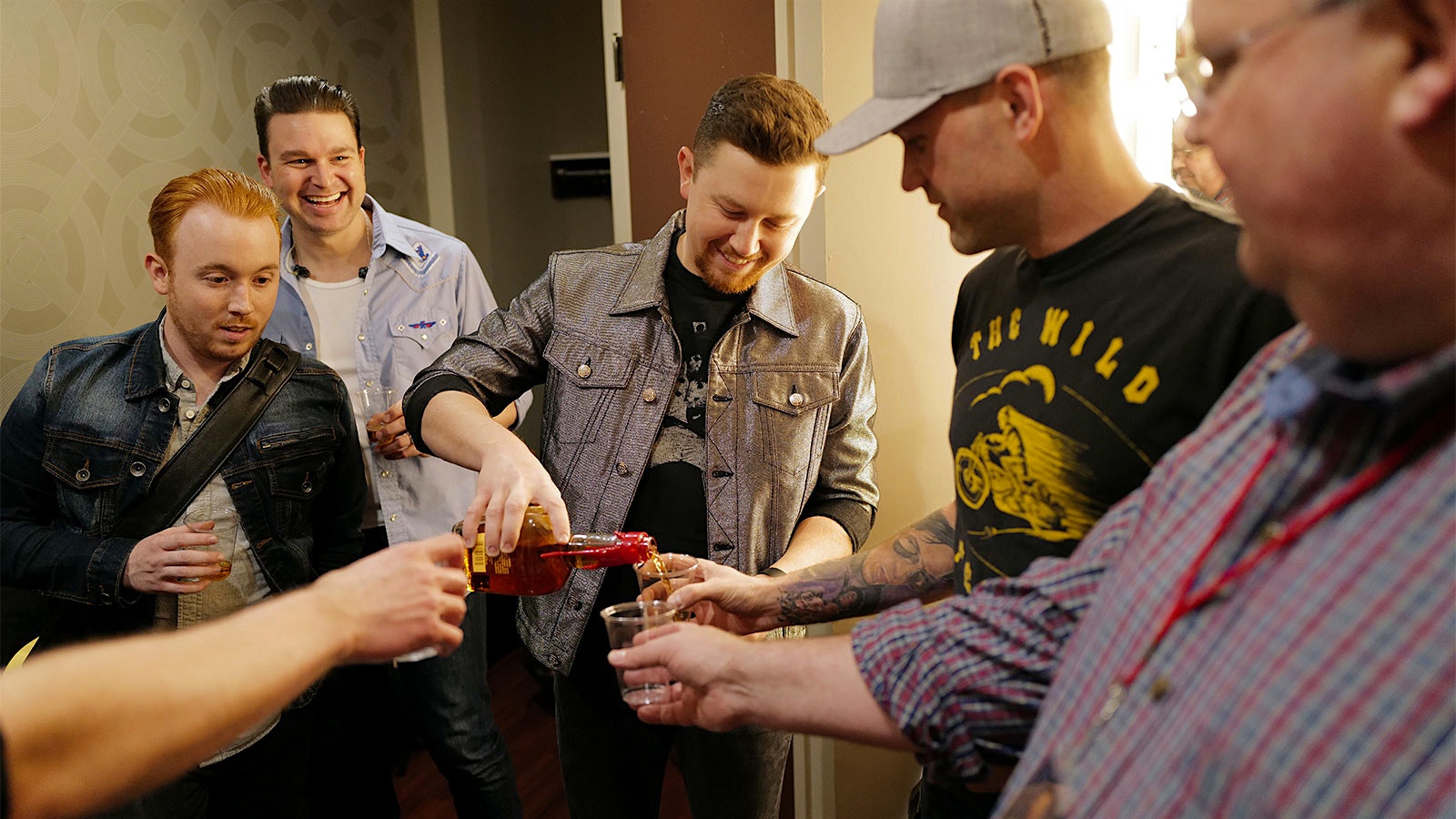Music star Scotty McCreery backstage after a concert, pouring bourbon for band members.